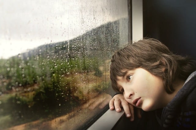 Middle Class Dadchild behavior problems and solutions sad boy with medium length brown hair leaning on a window sill while it rains outside