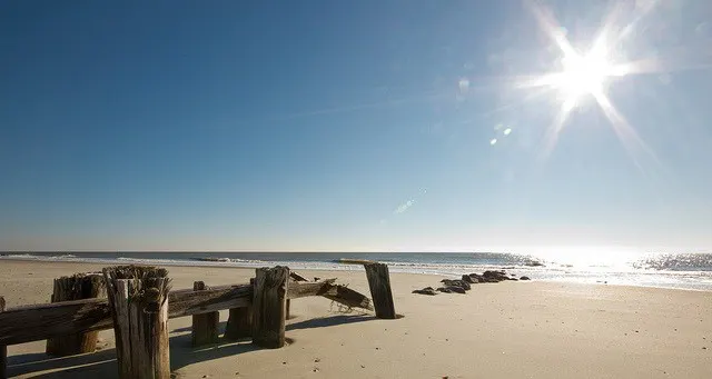 empty beach with the sun overhead and the remnants of an old dock on the sand affordable family vacation destinations Middle Class Dad 