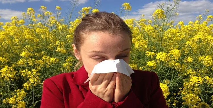 how to cure allergies naturally Middle Class Dad woman in a red top in a field of flowers sneezing into a tissue