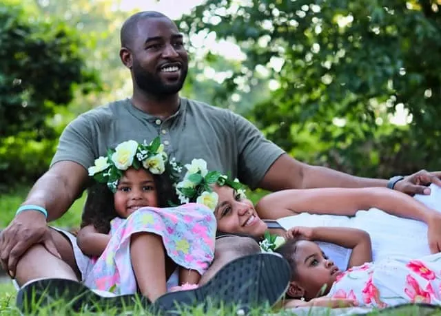 father, wife and daughters sitting in the grass smiling Middle Class Dad authoritative parenting examples