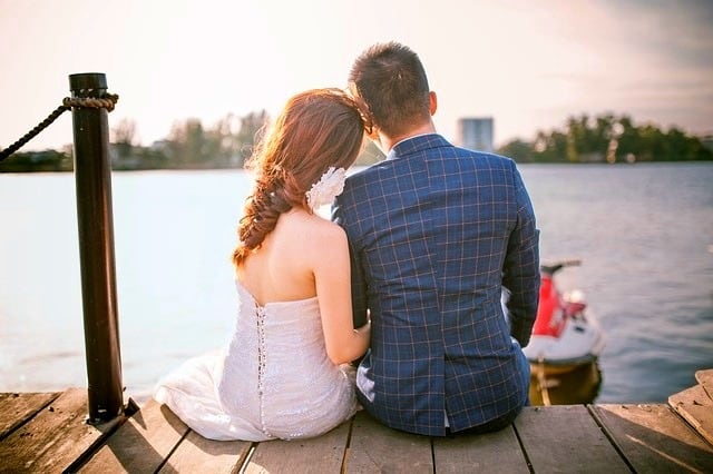restore intimacy in marriage Middle Class Dad woman in a wedding dress and a man in a blue suit sitting on a dock with a city in the distance on the other side of the water
