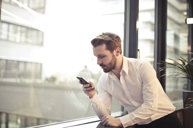 Middle Class Dad clingy guy young guy in a white button up shirt checing his phone in an office building