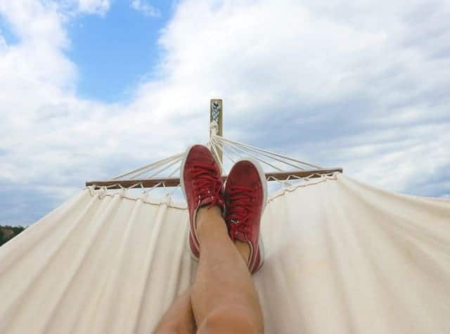 Middle Class Dad earn extra money on the side legs with red sneakers lounging on a hammock with blue sky and clouds in the background