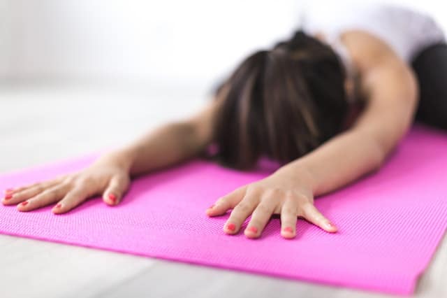Middle Class Dad yogic breathing benefits woman in child's pose on a pink yoga mat