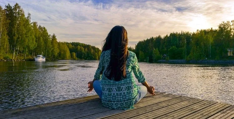 why go on a spiritual retreat Middle Class Dad woman meditating on a dock at the edge of a lake