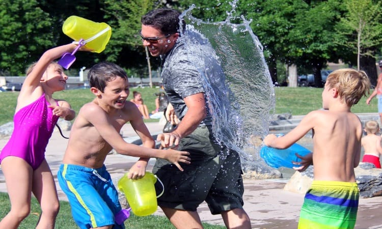 low-cost summer family fun ideas a bunch of kids dumping buckets of water on their dad in a park Middle Class Dad