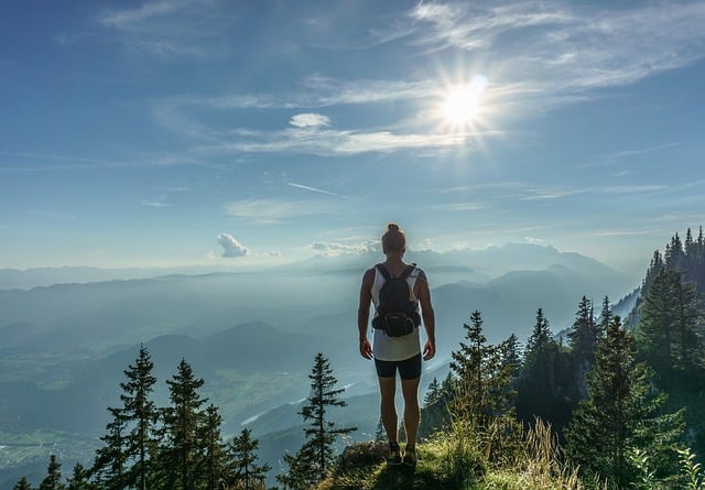 what is trekking all about? Middle Class Dad woman on the top of a tree lined mounatin looking out over a valley as the sun peaks through the clouds